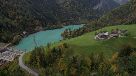 fantastic-close-up-aerial-shot-traveling-in-over-Mapragg-power-station-in-switzerland-and-surrounded-by-autumn-forests,-houses-and-a-beautiful-turquoise-lake