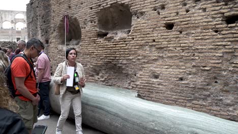 Guía-Turística-Femenina-Explicando-A-Los-Turistas-Sobre-La-Columna-De-Mármol-Dentro-Del-Coliseo-En-Roma.