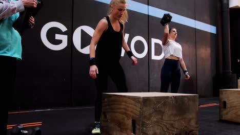 Eine-Junge-Blonde-Kaukasische-Frau-Springt-Während-Eines-Crossfit-Wettbewerbs-Namens-„Box-Jump“-Auf-Eine-Holzkiste.