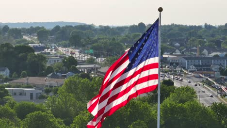 Towering-American-flag-moving-gently-in-the-breeze,-verdant-suburb-backdrop