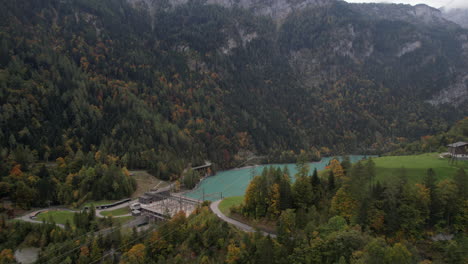 Fantástica-Toma-Aérea-Que-Viaja-Sobre-La-Central-Eléctrica-De-Mapragg-En-Suiza-Y-Está-Rodeada-De-Bosques-Otoñales-Y-Un-Hermoso-Lago-Turquesa.