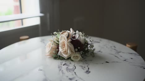Small-Wedding-Flower-Bouquet-Placed-On-A-Table-Nearby-The-Window-On-Daylight-With-Two-Wedding-Rings-On-Top