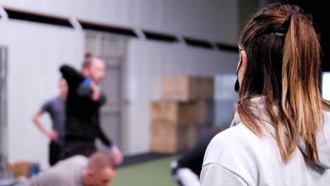 Subjektiver-Blick-Hinter-Eine-Junge-Frau-Mit-Schwarzer-Maske-Vor-Jungen-Sportlichen-Männern,-Die-Während-Ihrer-Crossfit-Sitzung-Gewichte-Mit-Den-Armen-Heben