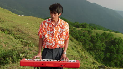 Static-shot-of-young-man-playing-the-piano-surrounded-by-hilly-terrain-covered-with-lush-green-vegetation-at-daytime