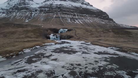 Drone-Shot,-Waterfalls-Under-Volcanic-Hills-in-Cold-Winter-Landscape-of-Iceland