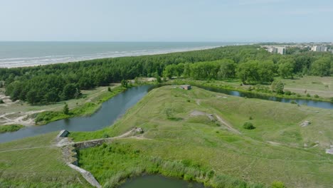 Aerial-establishing-view-of-abandoned-historical-concrete-seaside-fortification-buildings,-Southern-Forts-near-the-beach-of-Baltic-sea-in-Liepaja,-sunny-summer-day,-wide-drone-shot-moving-forward