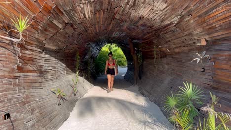 Eine-Junge-Frau-Im-Bikini-Geht-Durch-Einen-Holztunnel-Am-Strand-Von-Tulum-In-Der-Zona-Hotelera,-Selina-Hotel