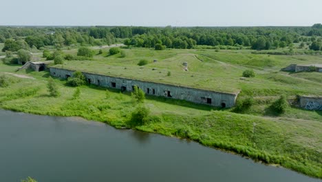 Aerial-establishing-view-of-abandoned-historical-concrete-seaside-fortification-buildings,-Southern-Forts-near-the-beach-of-Baltic-sea-in-Liepaja,-sunny-summer-day,-ascending-drone-dolly-shot
