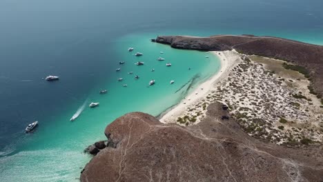 Drone-view-of-Playa-Balandra-in-La-Paz,-Mexico-with-yachts,-sailboats,-and-slow-motion-tilt-down