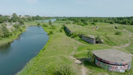 Aerial-establishing-view-of-abandoned-historical-concrete-seaside-fortification-buildings,-Southern-Forts-near-the-beach-of-Baltic-sea-in-Liepaja,-sunny-summer-day,-wide-drone-shot-moving-forward