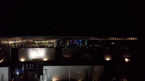 Drone-flying-away-from-a-luxurious-party-on-the-second-floor-of-the-Olympic-Museum-and-revealing-the-beautiful-town-of-Lausanne,-Switzerland-at-night