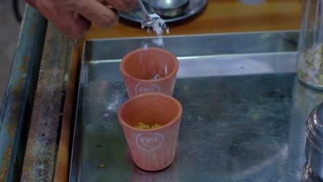 Scene-from-above-in-which-a-man-is-pouring-natural-herb-ingredients-into-two-clay-glasses-to-use-in-his-A2-milk-products