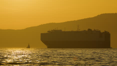 Silhouette-Eines-Frachtschiffs-Und-Eines-Kleinen-Segelboots-In-Der-Englischen-Bucht-Von-Vancouver---Sonnenuntergangshimmel