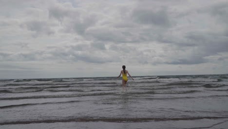 A-young-girl-in-a-yellow-swimsuit-runNing-into-the-ocean,-slow-motion