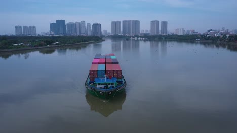 Container-boat-on-Saigon-river-from-aerial-view-on-sunny-day-from-front-angle-showing-revealing-Thao-Dien,-Ho-Chi-Minh-City-skyline