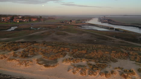 Rising-flight-from-Walberswick-beach-looking-towards-Walberswick-and-Southwold-harbour,-Suffolk-at-sunrise-with-the-moon-and-mist