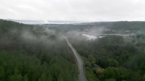 Aerial-drone-footage-of-single-highway-winding-through-a-lush,-foggy-rainforest