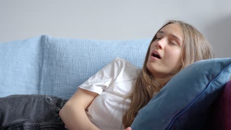 Young-brunette-use-TV-remote-and-yawning-while-on-home-sofa,-front-view