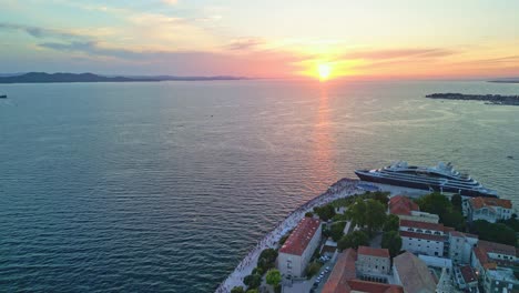 Sonnenuntergang-über-Zadar-Von-Oben,-Altstadtpromenade-Und-Architektonische-Installation.-Grüße-An-Die-Sonne-Mit-Daneben-Angedocktem-Kreuzer