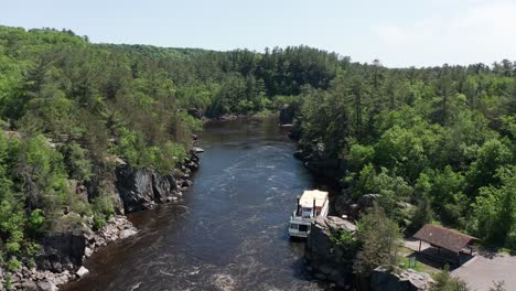 Aerial-descending-and-panning-shot-of-a-riverboat-docked-on-the-Saint-Croix-River-in-Taylors-Falls,-Minnesota