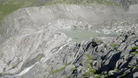 Waterfall-from-melting-Rhone-Glacier-ice,-Swiss-Alps,-aerial-drone-view