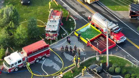 Firefighting-vehicles-at-the-explosion-site,-Fire-trucks-refilling-portable-and-collapsible-water-tanks,-Aerial-View