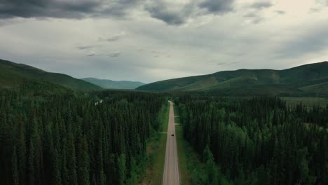 A-lone-vehicle-speeds-along-a-highway-amidst-a-green-forest-in-Alaska