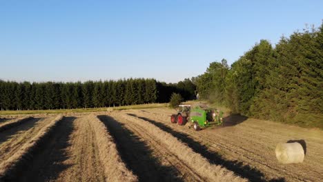 Tractor-pressing-hay-bales-in-Belgium,-filmed-by-drone