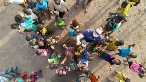 Hand-landing-a-drone-in-an-African-village,-while-African-children-jump-to-it