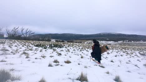 Una-Toma-Amplia-De-Un-Paisaje-Salvaje-De-Montaña-Nevada-Con-Un-Explorador-Tradicional-Del-Siglo-XIX-Caminando-Con-Raquetas-De-Nieve