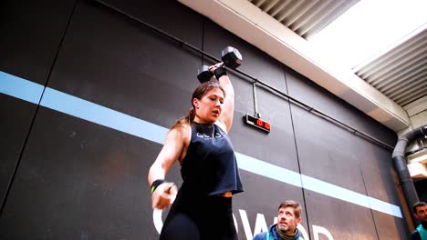 slowmotion-video-of-an-athletic-woman-during-a-crossfit-session-lifting-a-weight-with-one-hand,-a-crouching-man-watches-her