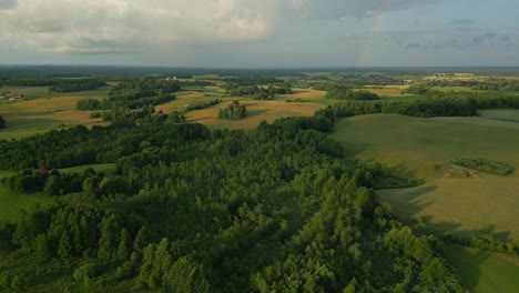 The-drone's-camera-slowly-tilts-down-a-landscape-full-of-fields-of-meadows-and-forests-with-a-rainbow-in-the-background