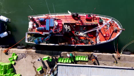 Fishermen-unloads-fish-from-moored-trawler-at-harbor,-top-down-aerial