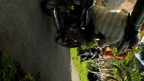 Vertical-super-slow-motion-handheld-shot-of-a-balinese-construction-worker-on-a-moving-scooter-with-bamboo-canes-going-to-the-construction-site-on-bali-indonesia