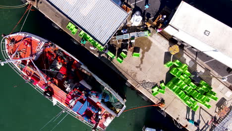 Aerial-riser-above-fishing-vessel-moored-on-harbor-wall-unloading-its-catch
