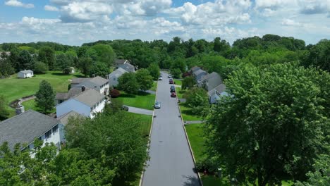 Aerial-backwards-shot-of-American-housing-area-with-wide-road-and-driving-vehicle-in-summer