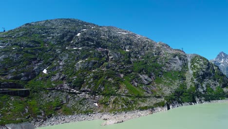 Drone-Aéreo-Hacia-Atrás-Disparado-Sobre-Un-Camino-Sinuoso-A-Lo-Largo-De-La-Ladera-De-La-Carretera-De-Alta-Montaña-Grimselpass-En-Los-Hermosos-Alpes-Suizos,-Suiza-En-Un-Día-Soleado