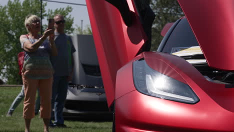 Old-Woman-Taking-Pictures-Of-Red-Chevrolet-Corvette-C7-Using-Mobile-Phone-During-Car-Show