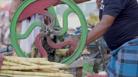 Sugercane-juice-seller-grinding-and-squeezing-sugercane-in-machine-to-extract-juice-in-hot-summer-season,-slow-motion-shot