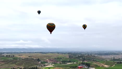 Hot-air-balloons-floating-over-Temecula,-California,-Rising-aerial-view-overlooking-colourful-morning-landscape