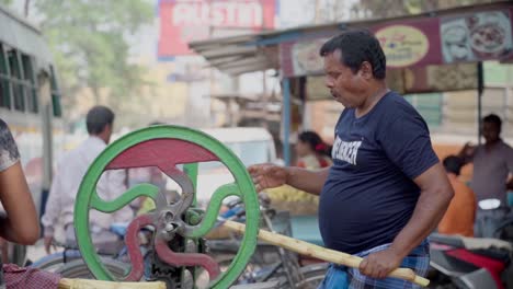 Indian-fruit-juice-seller-extracting-juice-from-sugercane-by-grinding-machine-in-hot-summer-season,-slow-motion-shot