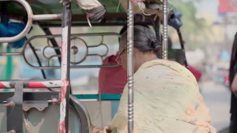 Old-Indian-woman-getting-inside-electric-rickshaw,-busy-indian-road,-slowmotion-shot