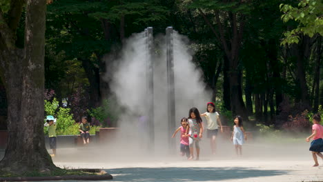 Grupo-De-Niños-Refrescándose-En-Un-Caluroso-Día-De-Verano-Bajo-Un-Sistema-De-Enfriamiento-Por-Goteo-De-Microflujo-En-El-Parque-Público-Bosque-Ciudadano-De-Yangjae