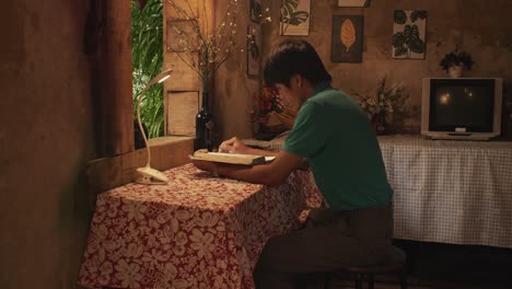 Young-Asian-male-reads-a-book-at-a-desk-in-a-rustic-room