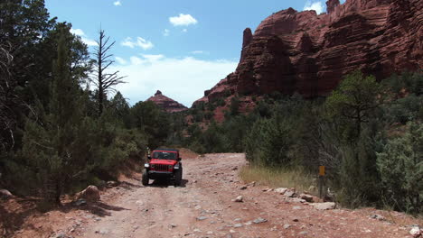 Aerial-view-of-a-jeep-driving-on-a-dirt-road-in-middle-of-mountains-of-Sedona,-USA