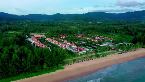 An-aerial-shot-of-beach-surrounded-by-a-resort-area-and-sea-under-the-sunlight,-Panorama-aerial-view-of-a-beach-in-Phuket,-Thailand