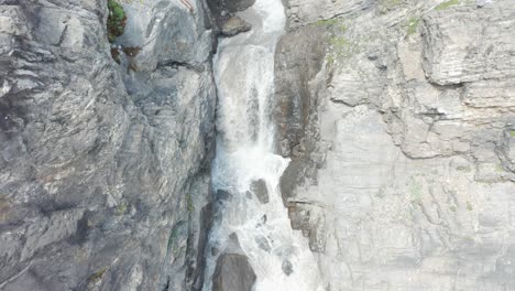 Blick-Aus-Der-Vogelperspektive-Auf-Einen-Kleinen-Wasserfall,-Der-Einen-Felsigen-Berg-Hinunterströmt