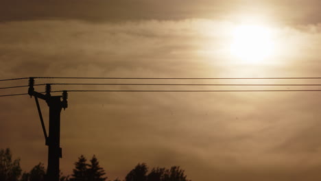 Silhouette-of-electricity-lines-against-vivid-orange-golden-hour-sky,-telephoto