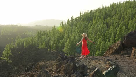 Carefree-young-woman-rises-arms-in-front-of-wonderful-forest-park,-golden-hour