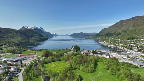 Sjoholt-and-Orskog-along-road-E39-underway-to-Alesund-in-western-Norway---Rising-summer-aerial-while-moving-slowly-ahead-over-lush-green-landscape-and-looking-at-fjord-Orskogvika